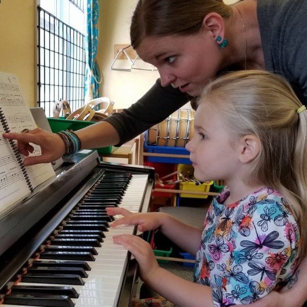 MYC teacher pointing at music notes while MYC student plays the piano